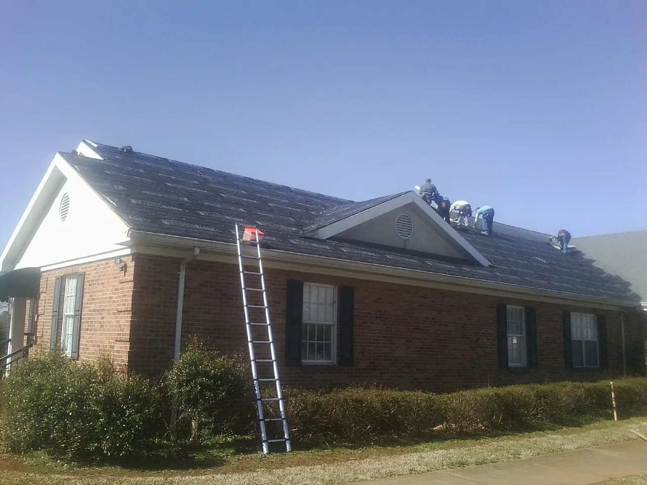 Crew tearing shingles off a brick ranch roof with a ladder set — Metal Roof Repair work by our crew in Gillette