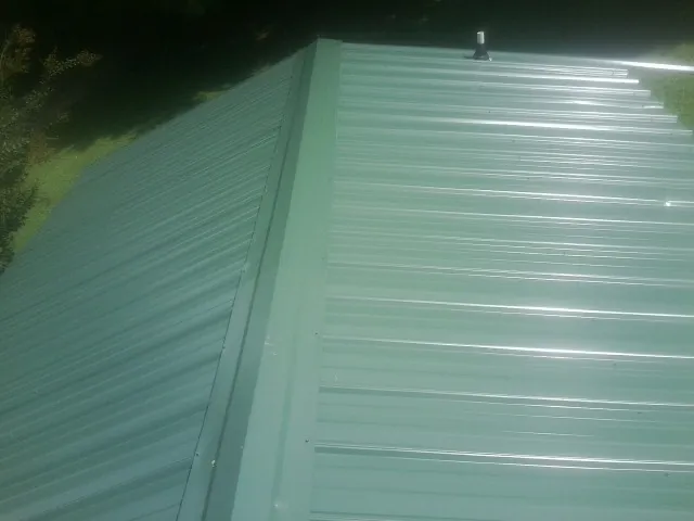 New green metal panels meeting at the ridge of a roof — Flat Roof Repair work by our crew in Gillette